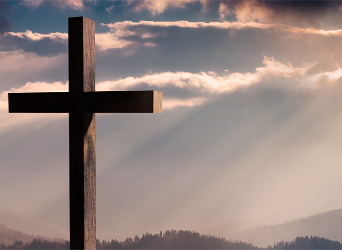 A cross is shown against the sky with clouds.