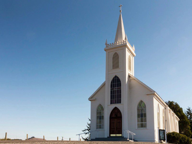 A white church with a steeple and a cross on top.